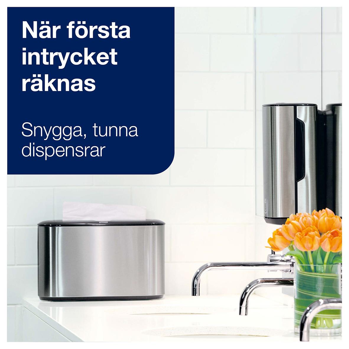 Dispenser för pappershanddukar i rostfritt stål på köksvägg med blomma och handfat