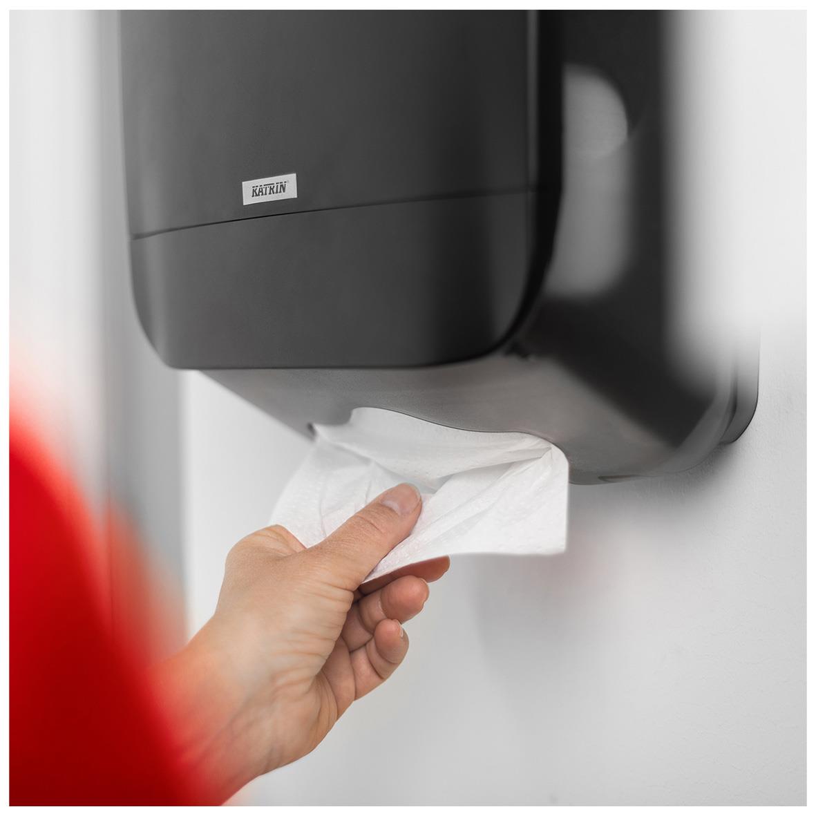 Hand som tar ett papper från en vit Katrin handduksdispenser