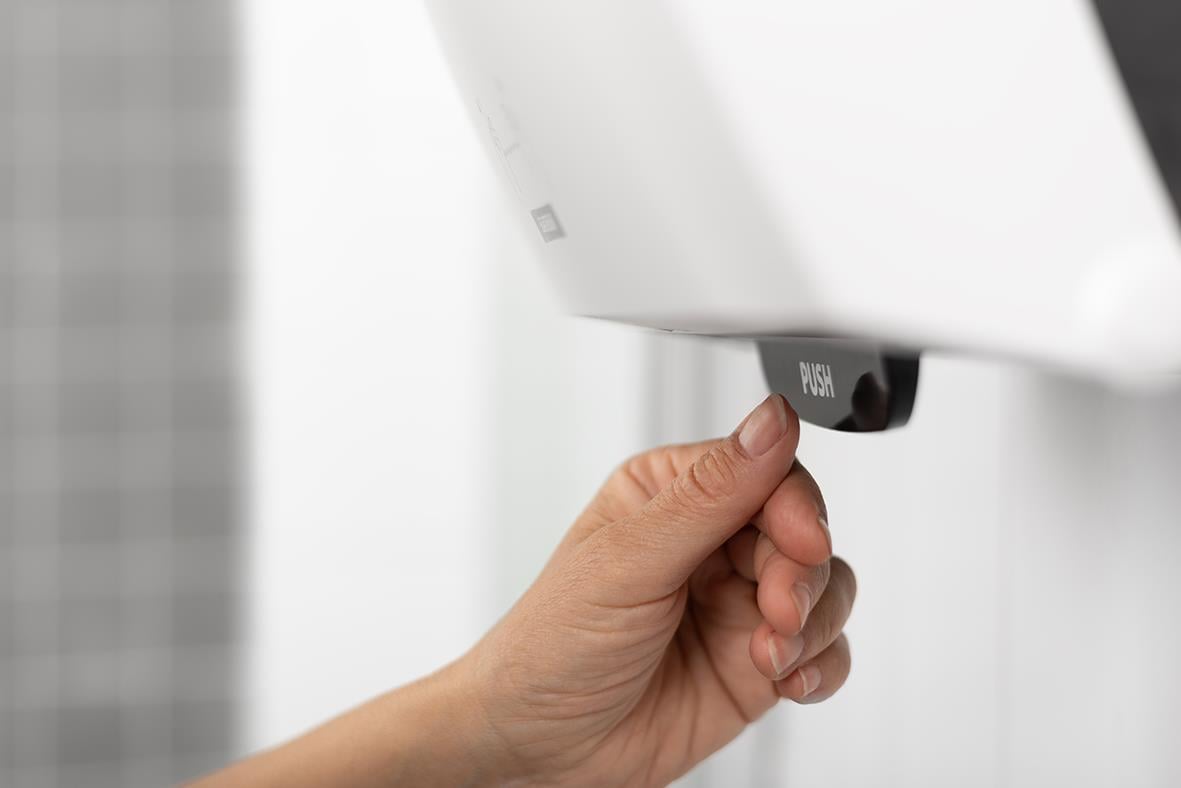 Hand som tar ett papper från Katrin System M2 vit pappershanddukspdispenser