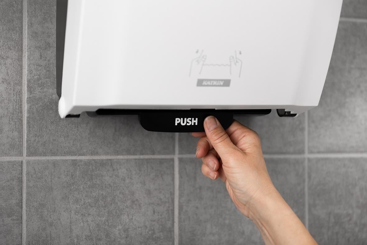 Hand som trycker på dispenser för pappershanddukar Katrin System M2 Vit