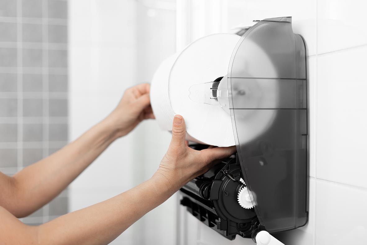 Person som installerar eller fyller Katrin System M2 pappershandduksdispenser i vitt