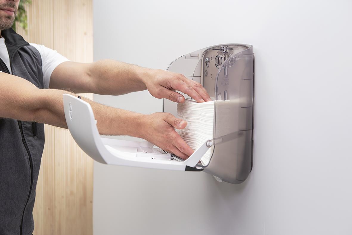 Person som använder Katrin S vit pappershanddukspdispenser på vägg