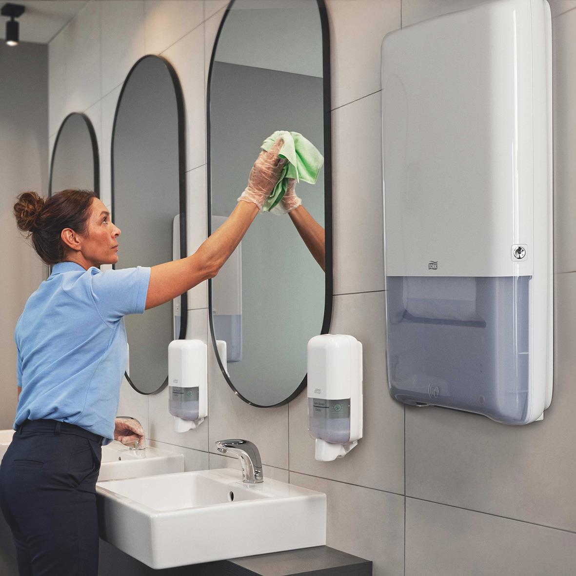 Person torkar spegel med trasa framför handfuktare i badrum