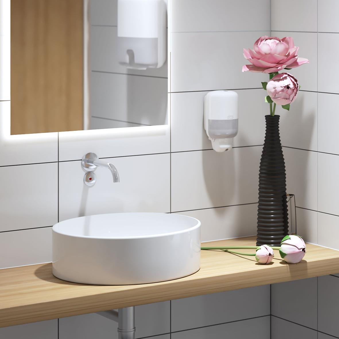 Vitt handfat på träbänk med rosa blommor i svart vas och spegel i badrum med vita väggar