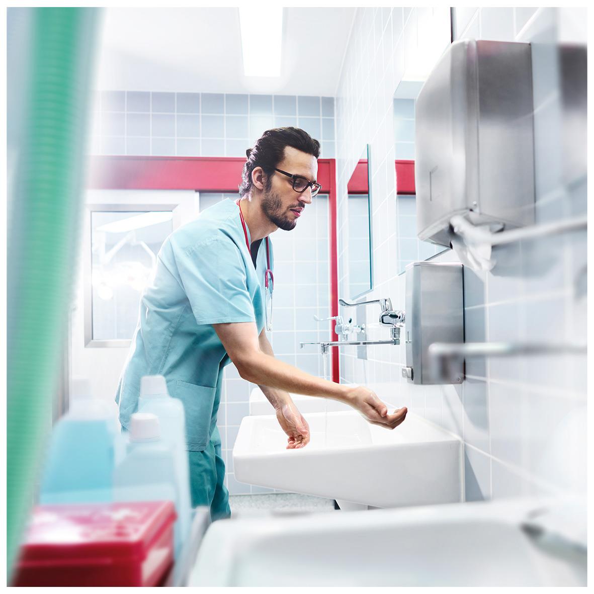Man i sjukhuskläder använder handdispenser för pappershanddukar i ett sjukhus eller klinikmiljö