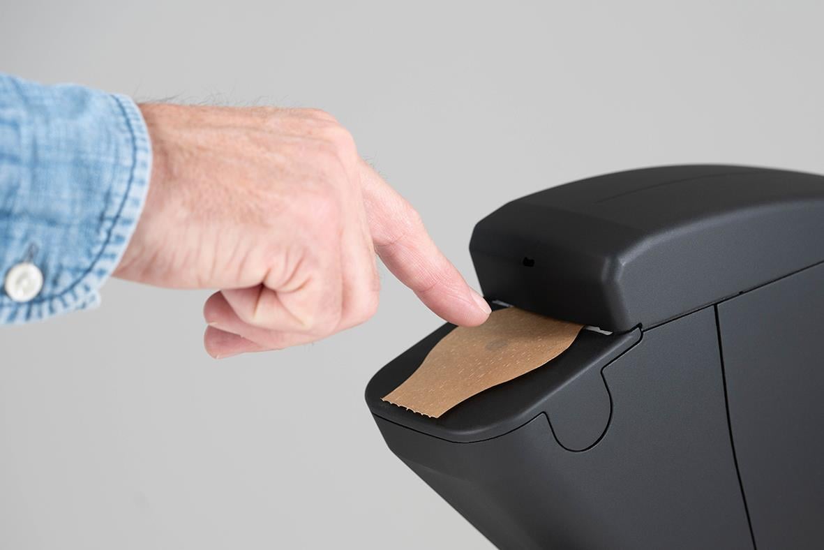 Svart dispenser med fingeravtrycksskydd och papper, användarens finger trycker på skivan