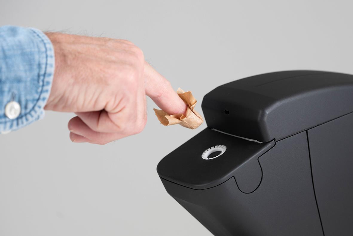 Väggfäste till svart dispenser för papper, mått 138x80x63mm, person som fyller på papper