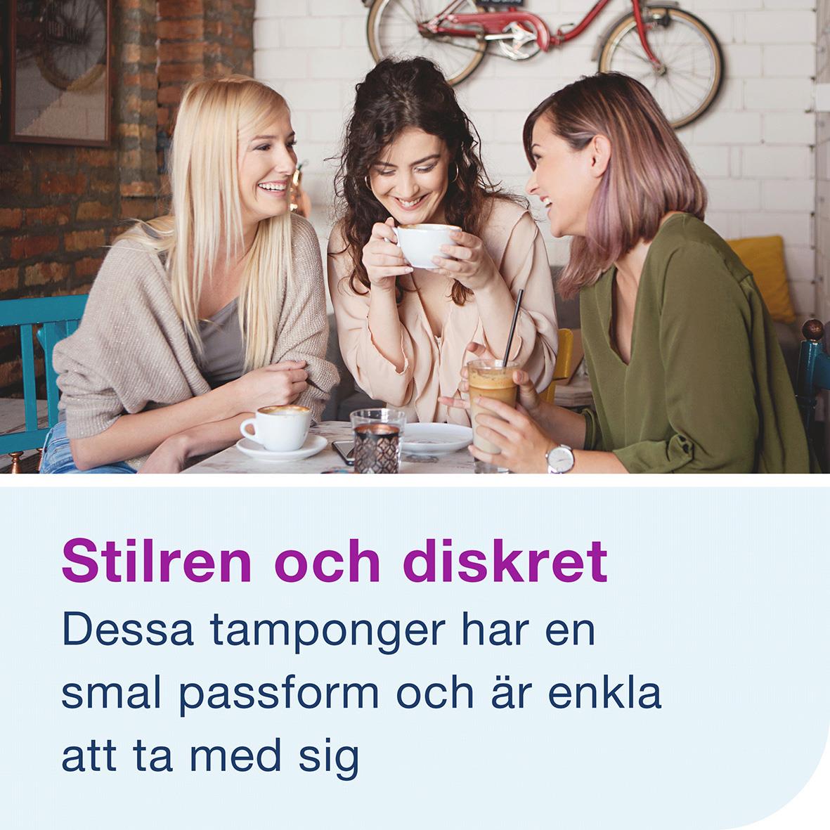 Tre kvinnor som skrattar och pratar på ett café, en av dem håller en skål, i bakgrunden en vit vägg med en cykel