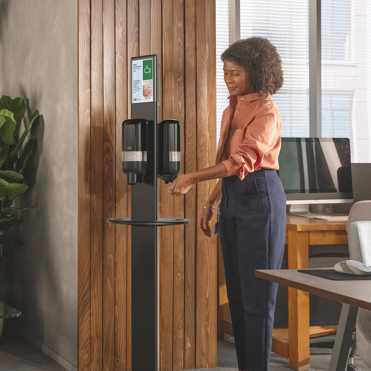 Kvinna använder handdesinfektionsstation med digital skärm i kontorsmiljö