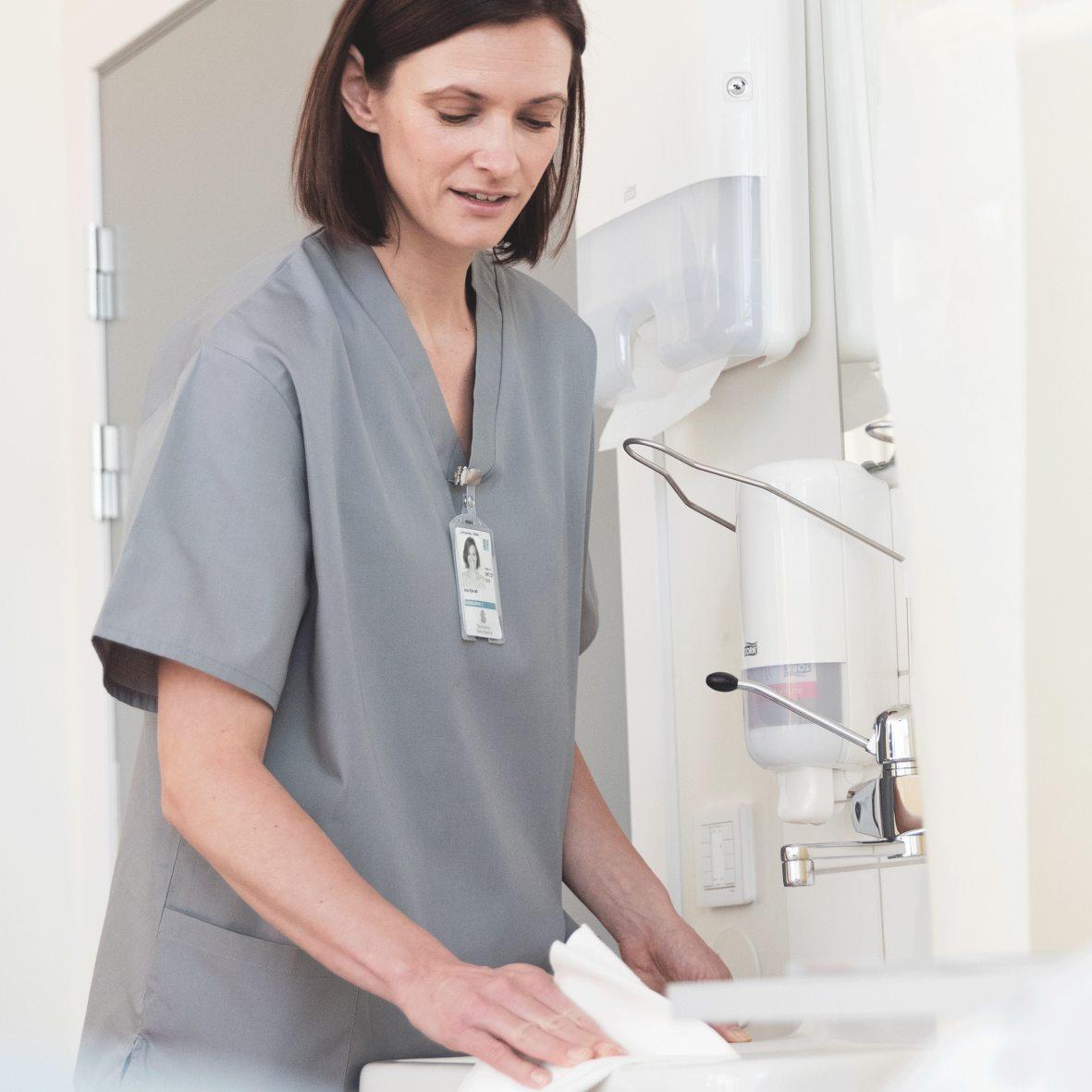 Kvinna i grå arbetskläder använder handdesinfektion i ett medicinskt miljö