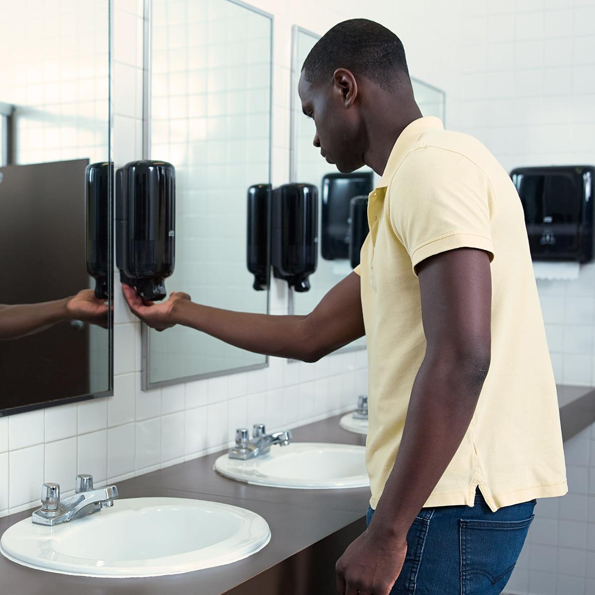 Man använder svart skumdispenser Tork S4 i en offentlig toalettmiljö