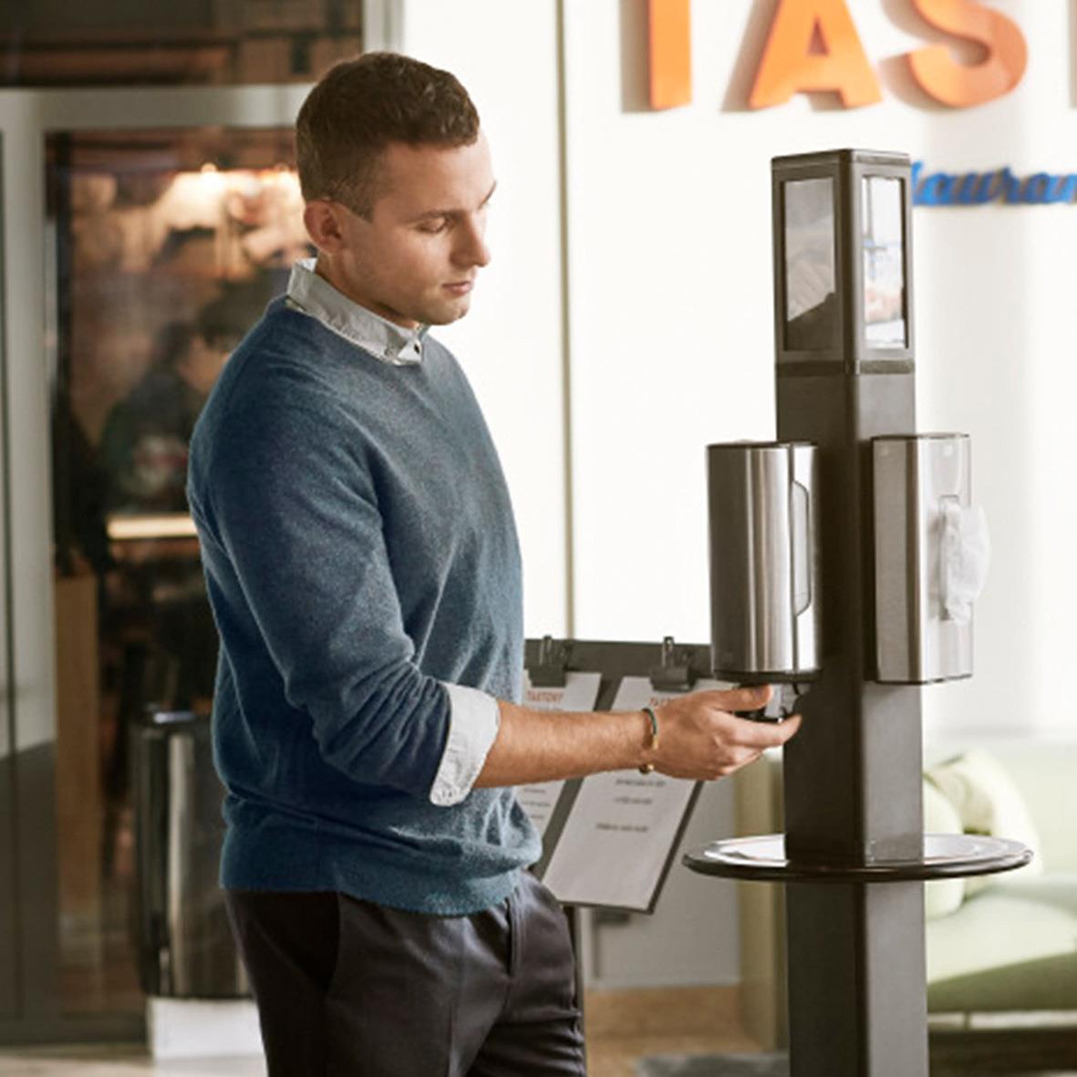 Man använder en handdesinfektionsstation med hygienställ i en offentlig miljö