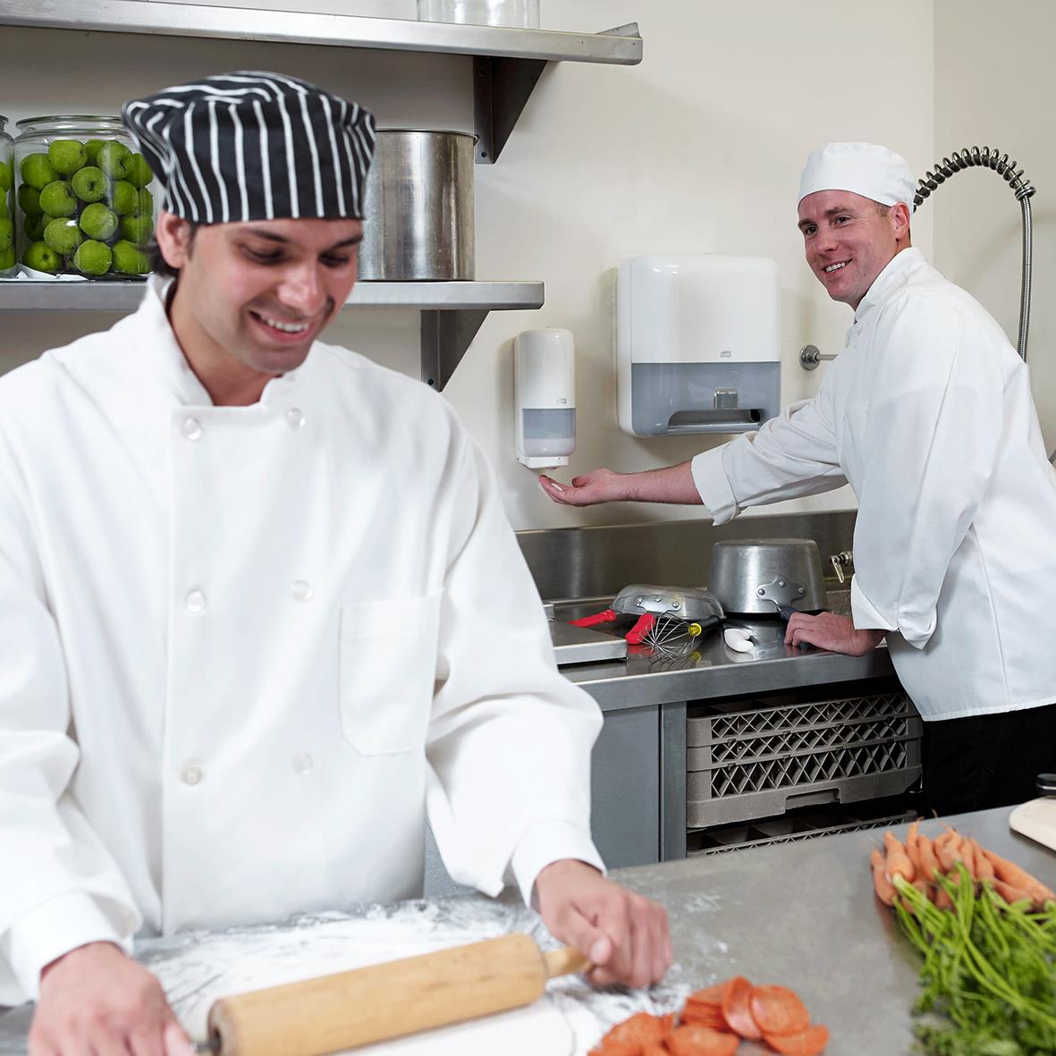 Två kockar i kök, en med svart och vit keps, bakar eller förbereder mat vid ett köksbord