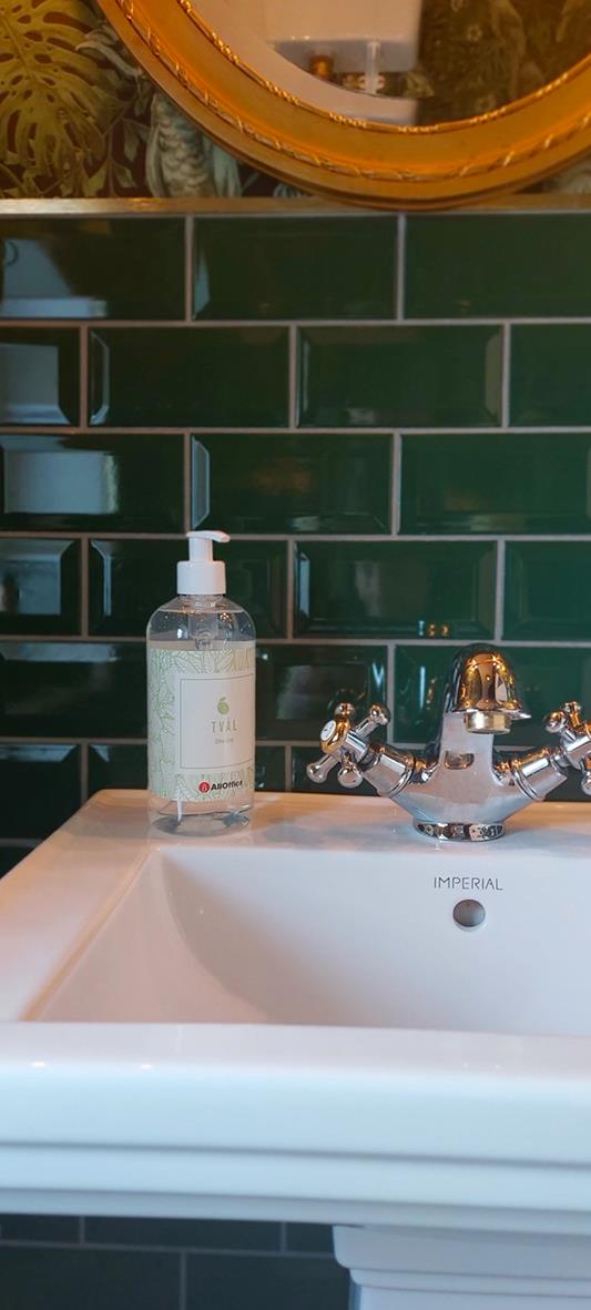 Flytande tvål i pumpflaska på handfat framför gröna kakelplattor