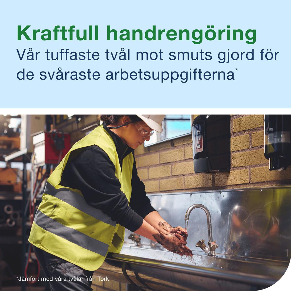 Person tvättar händer med flytande tvål i industriell miljö, bär reflexväst och skyddshjälm