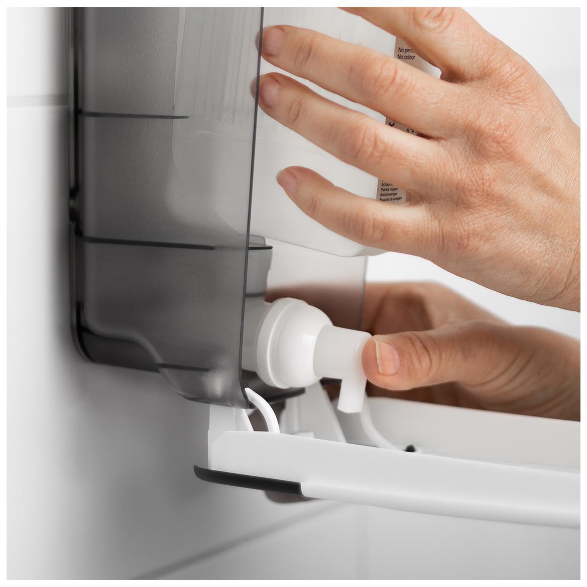 Hand som trycker på vit Katrin tvål dispenser på vägg