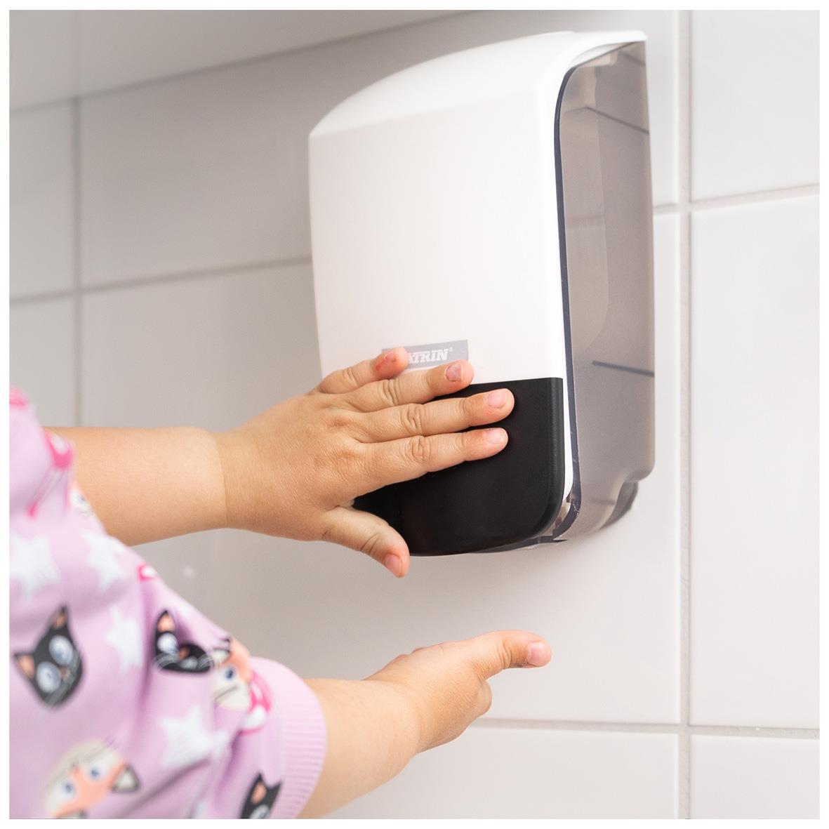 Vit Katrin tvål dispenser på vägg, barn som använder den