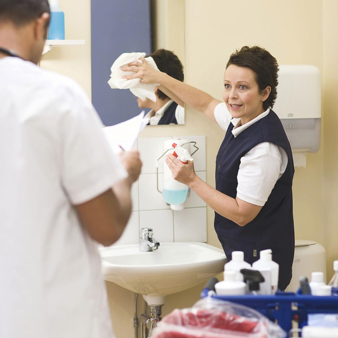 Person som torkar ett handfat med en vit tvättlapp i ett vårdmiljö