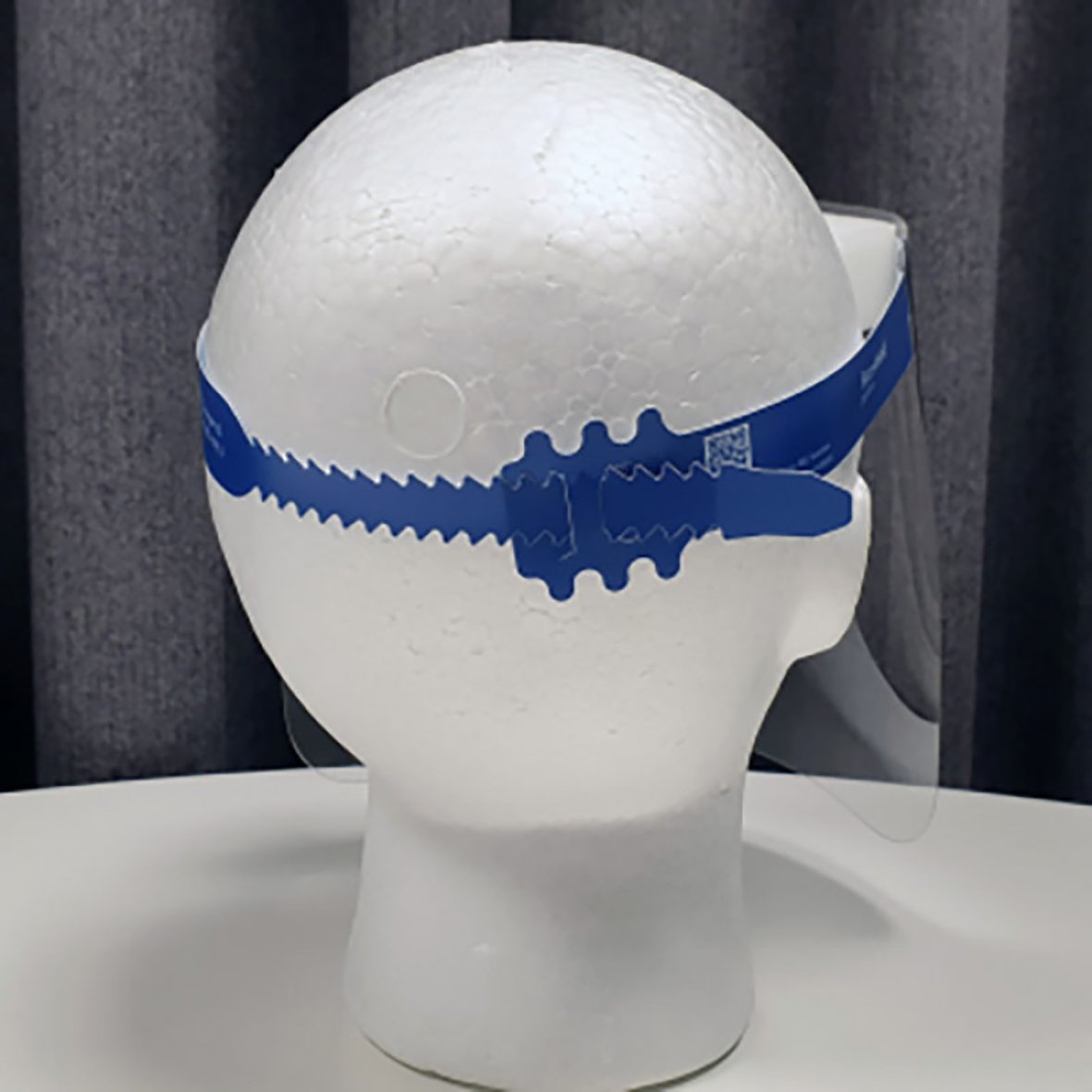 Skyddsvisir komplett med blå band och justerbar rem på en vit huvudmodell