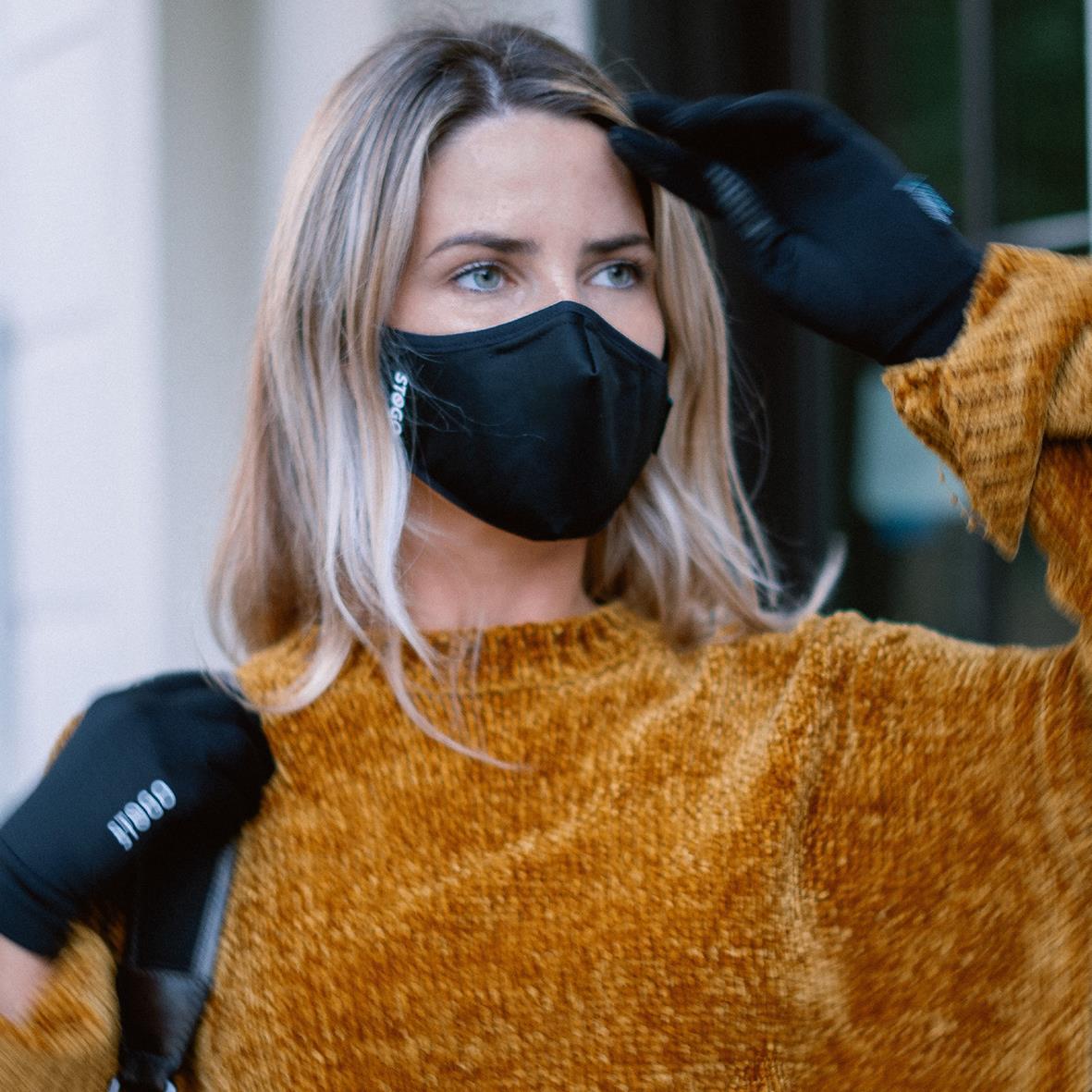 Kvinna bär svart munskydd och handskar, utomhus, i höstkläder