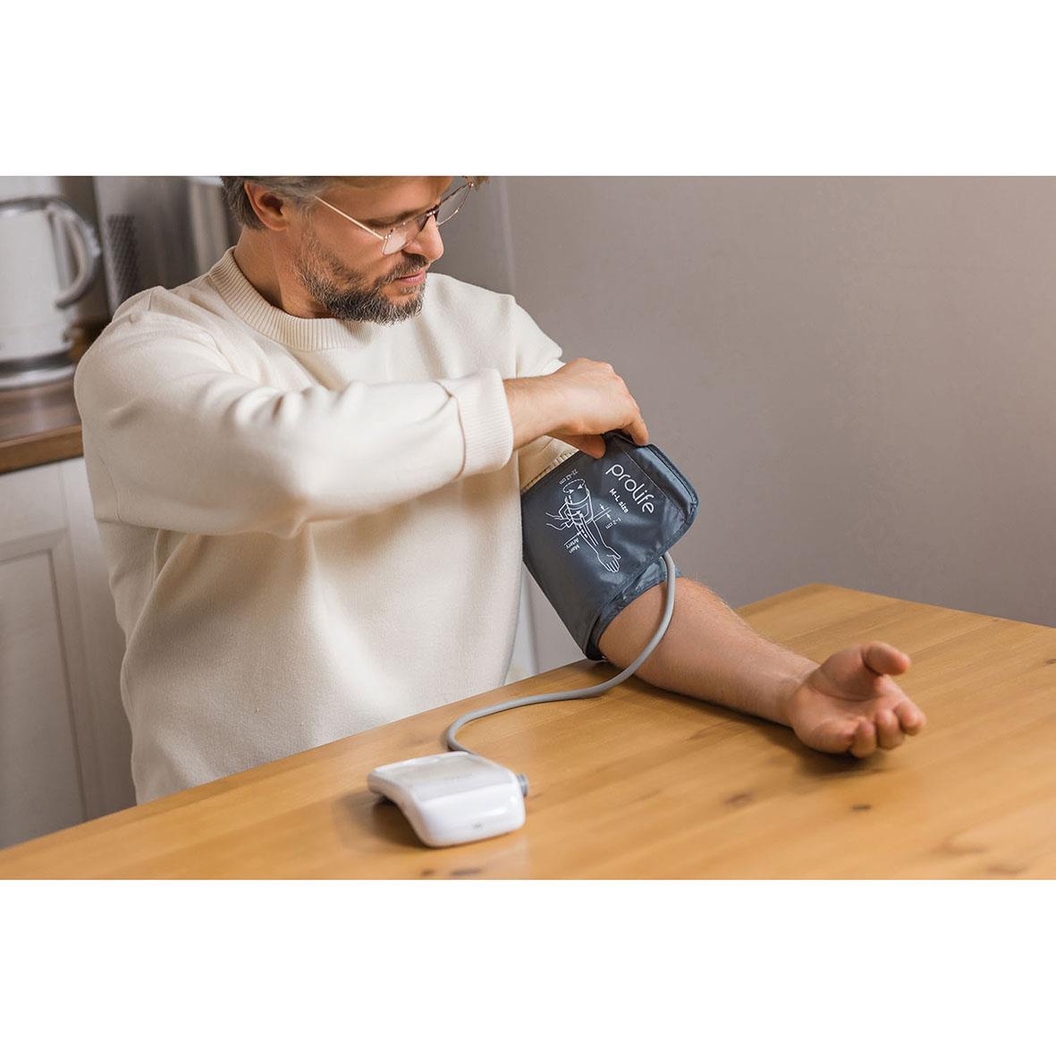 Man använder blodtrycksmätare Prolife Digital PA5 Comfort på armen vid ett bord