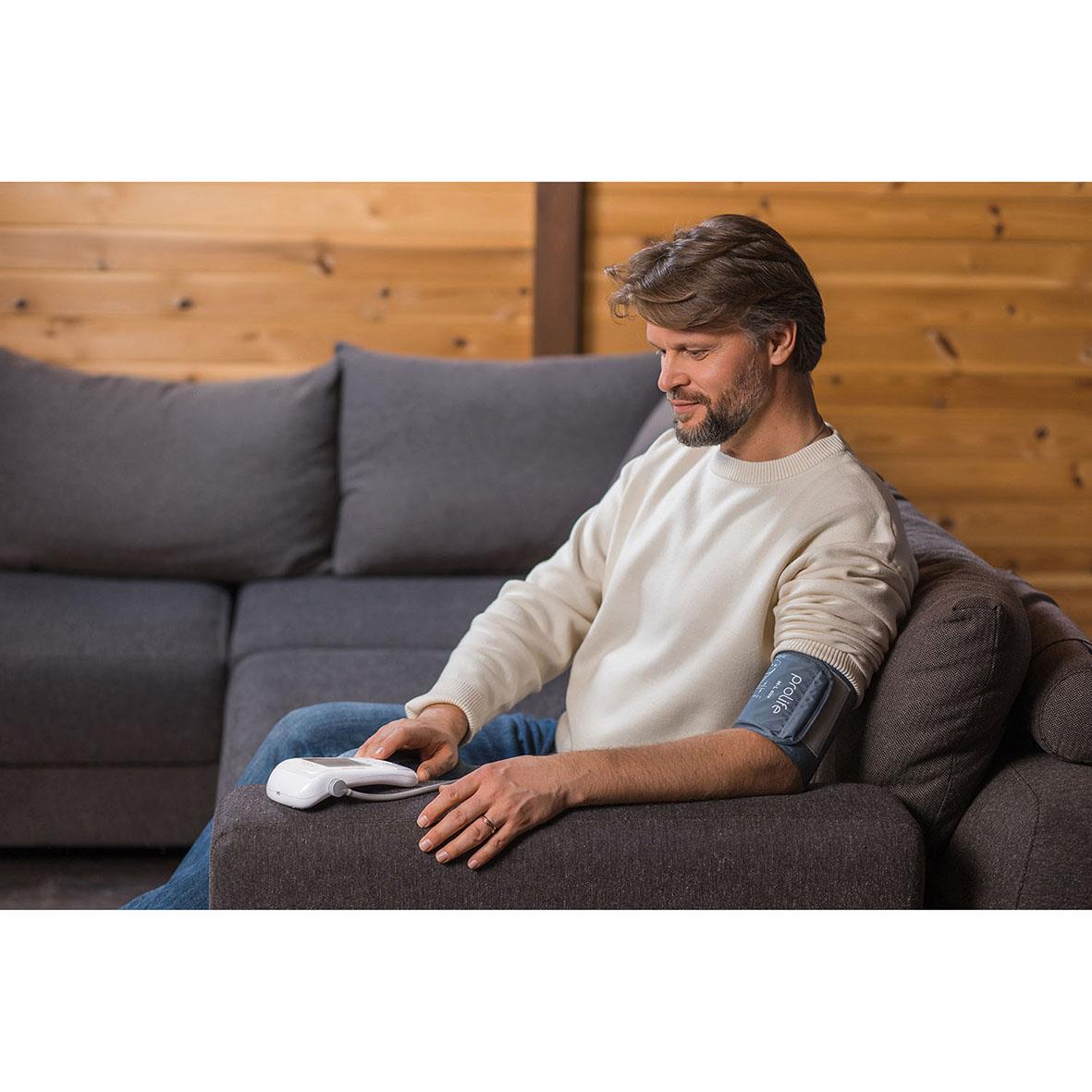 Man använder blodtrycksmätare Prolife Digital PA5 Comfort på armen medan han sitter i soffan