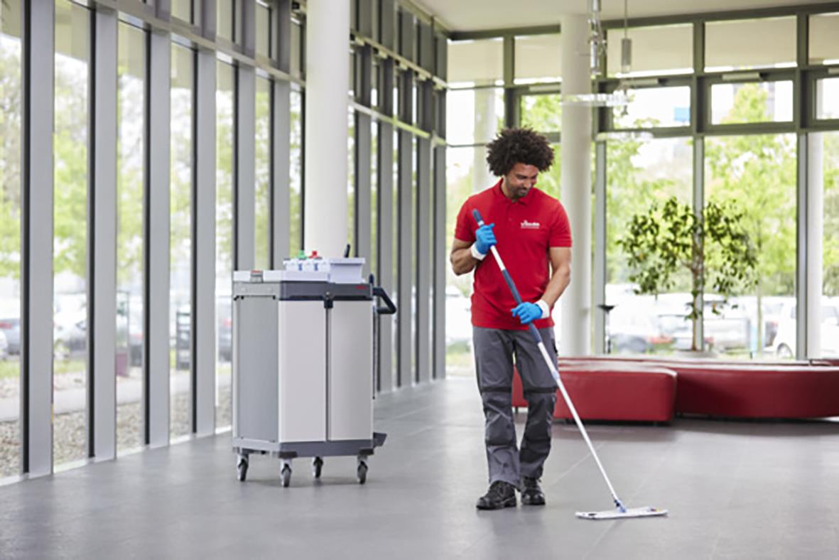 Man använder Vileda r-MicroLite Max 30cm kombimopp i ett modernt inomhusmiljö med stora fönster och gröna växter