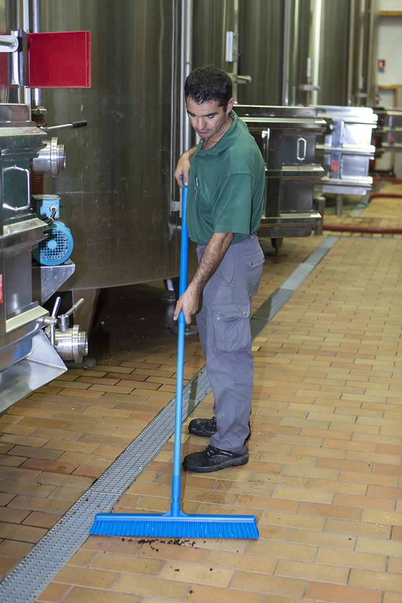 Man sopar golv med blå sopborste i industriell miljö
