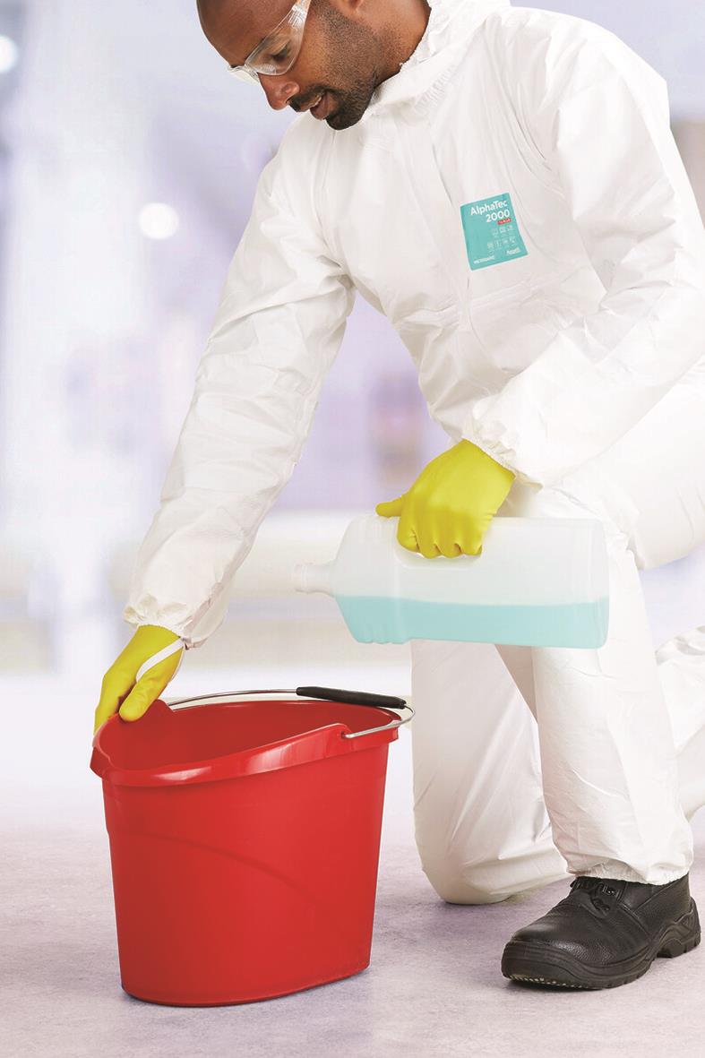 Person i skyddskläder och gula handskar hanterar en röd hink i ett laboratorium eller renrum