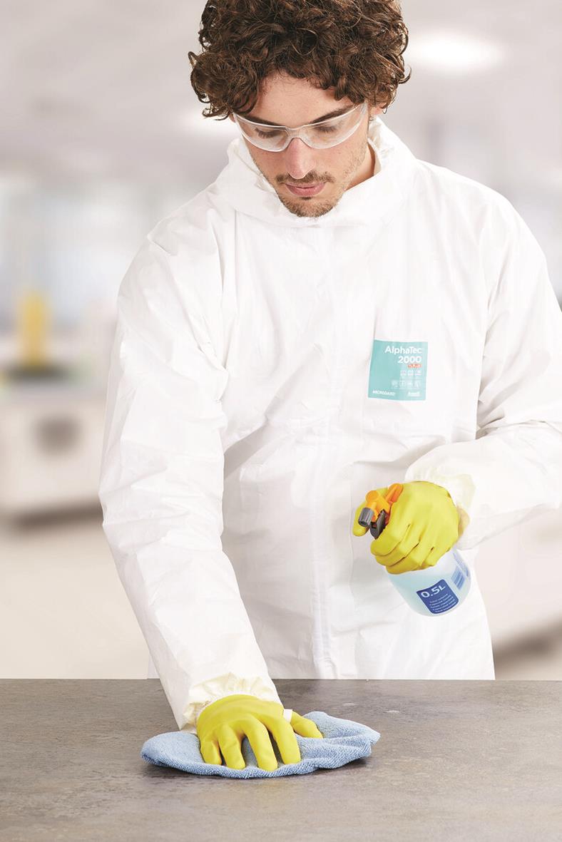 Person i skyddskläder och gula handskar torkar ett bord med trasa i ett laboratorium eller kök