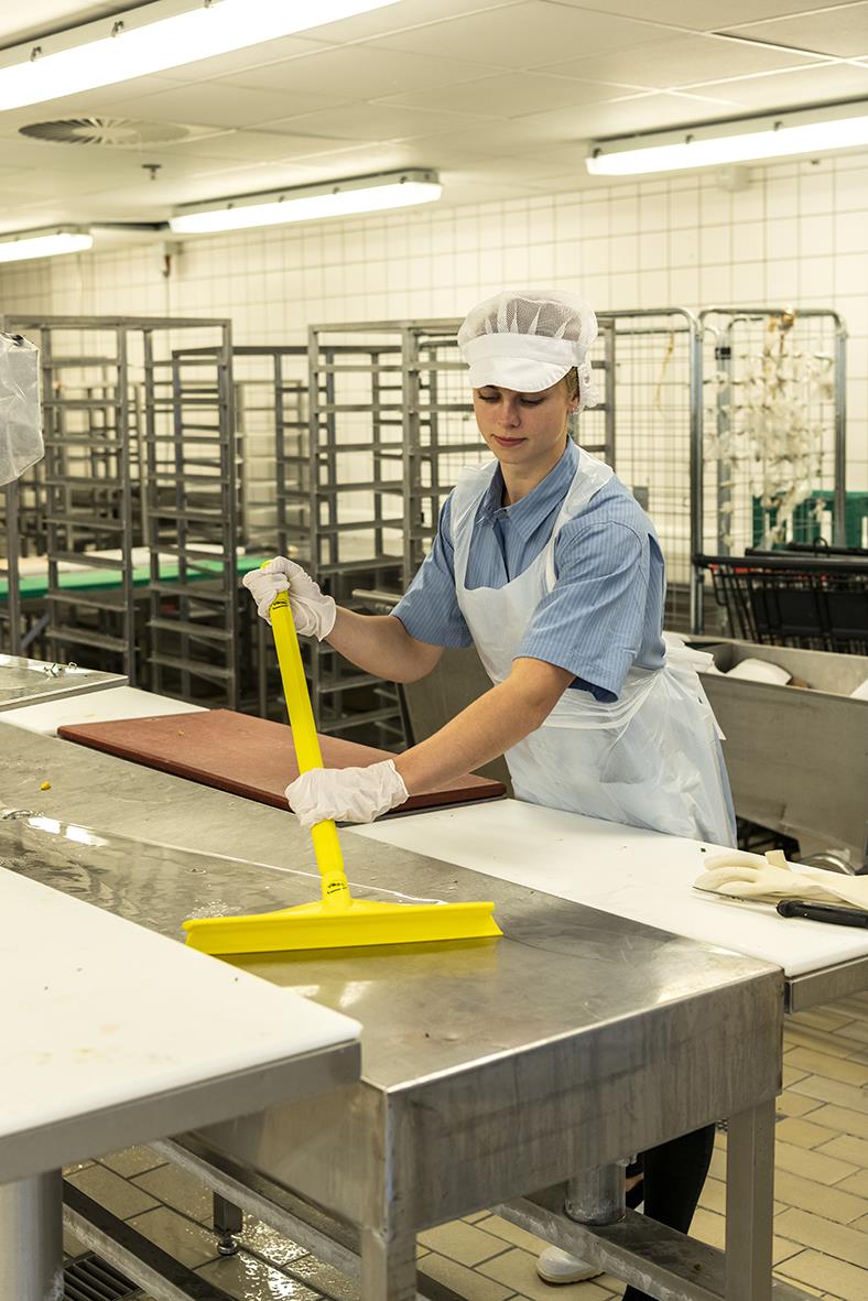 Person som använder en gul golvskrapa i ett industriellt kök eller fabrikslokal