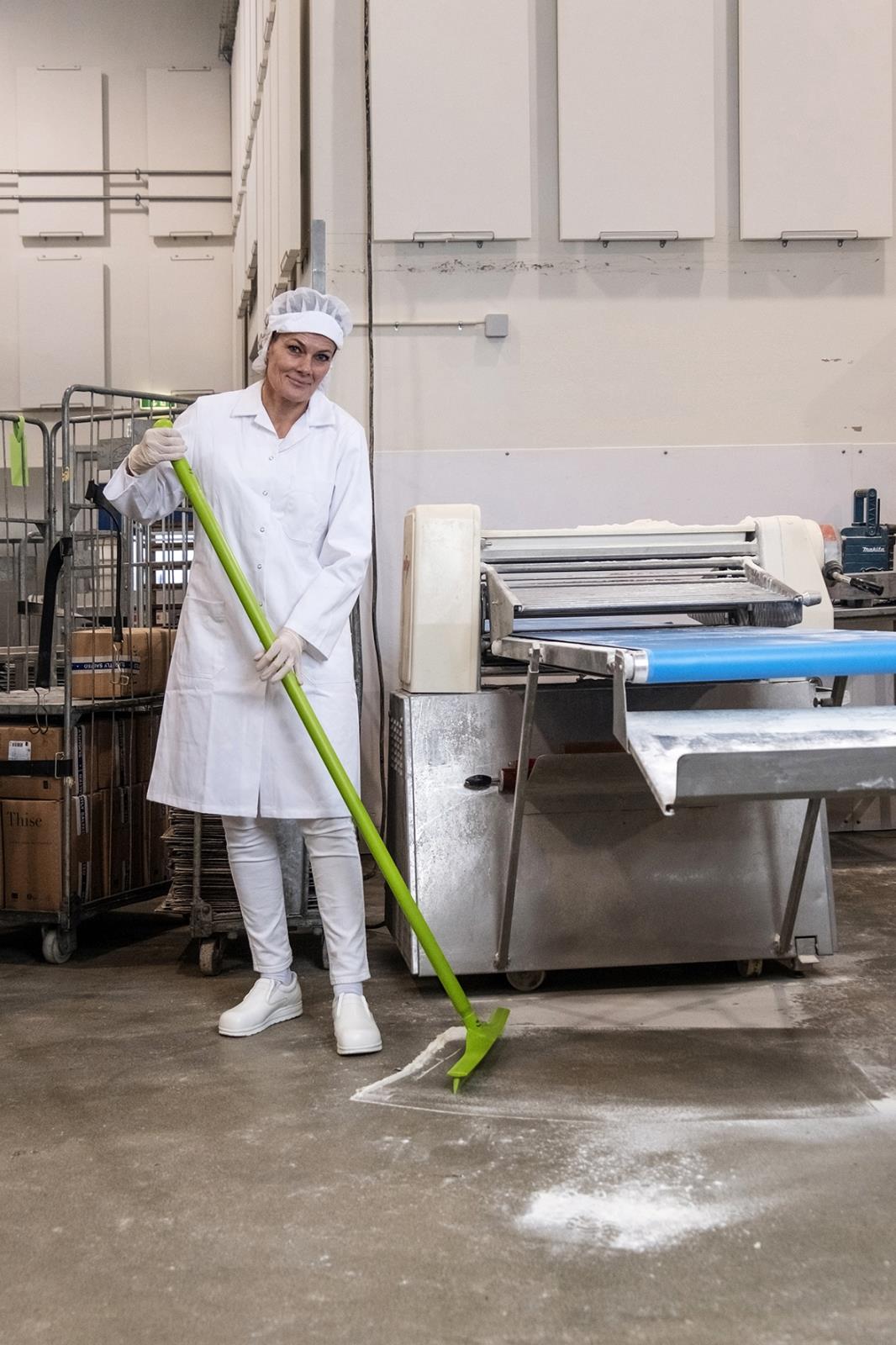 Person i arbetskläder använder en blå golvskrapa för att rengöra golvet i ett industriellt utrymme