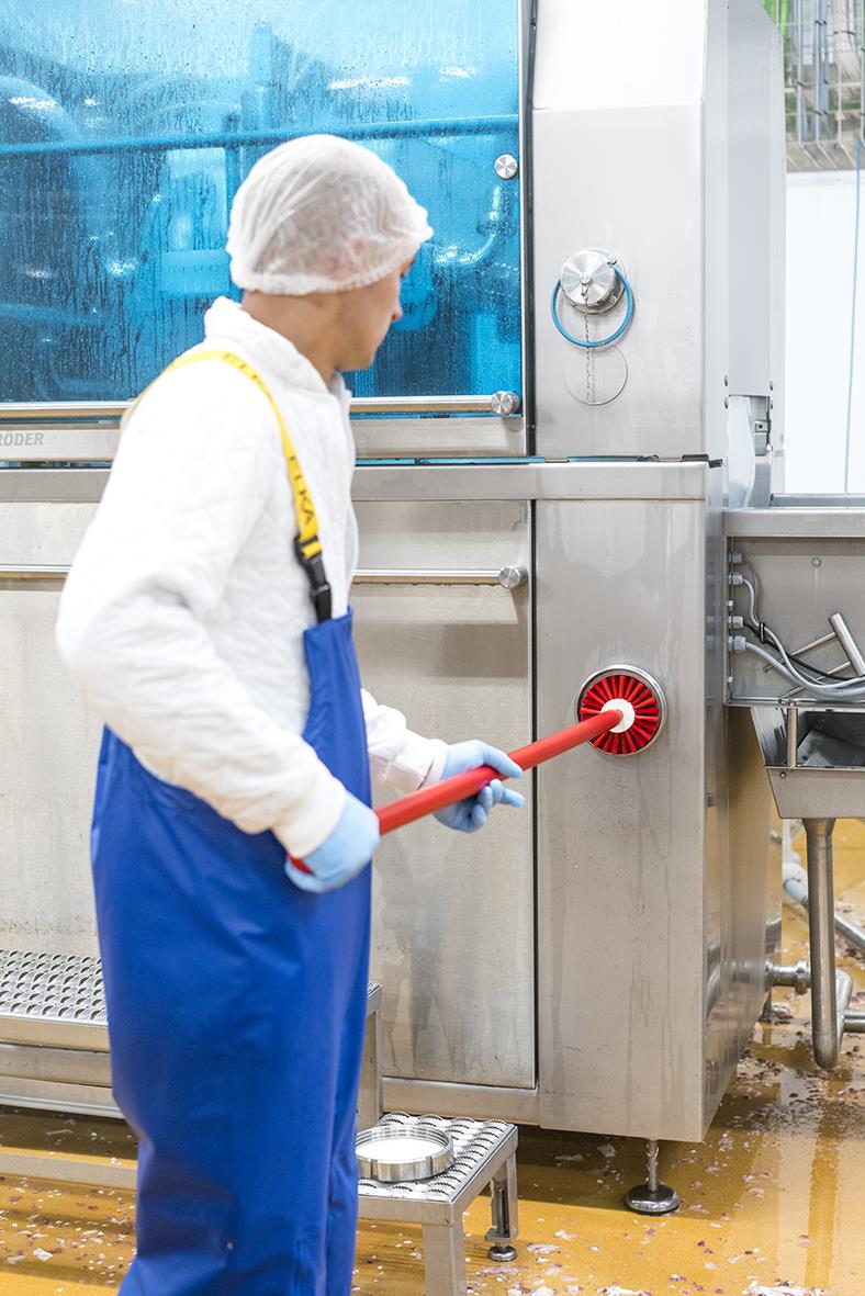 Person i skyddskläder rengör maskin med rött verktyg i industriell miljö