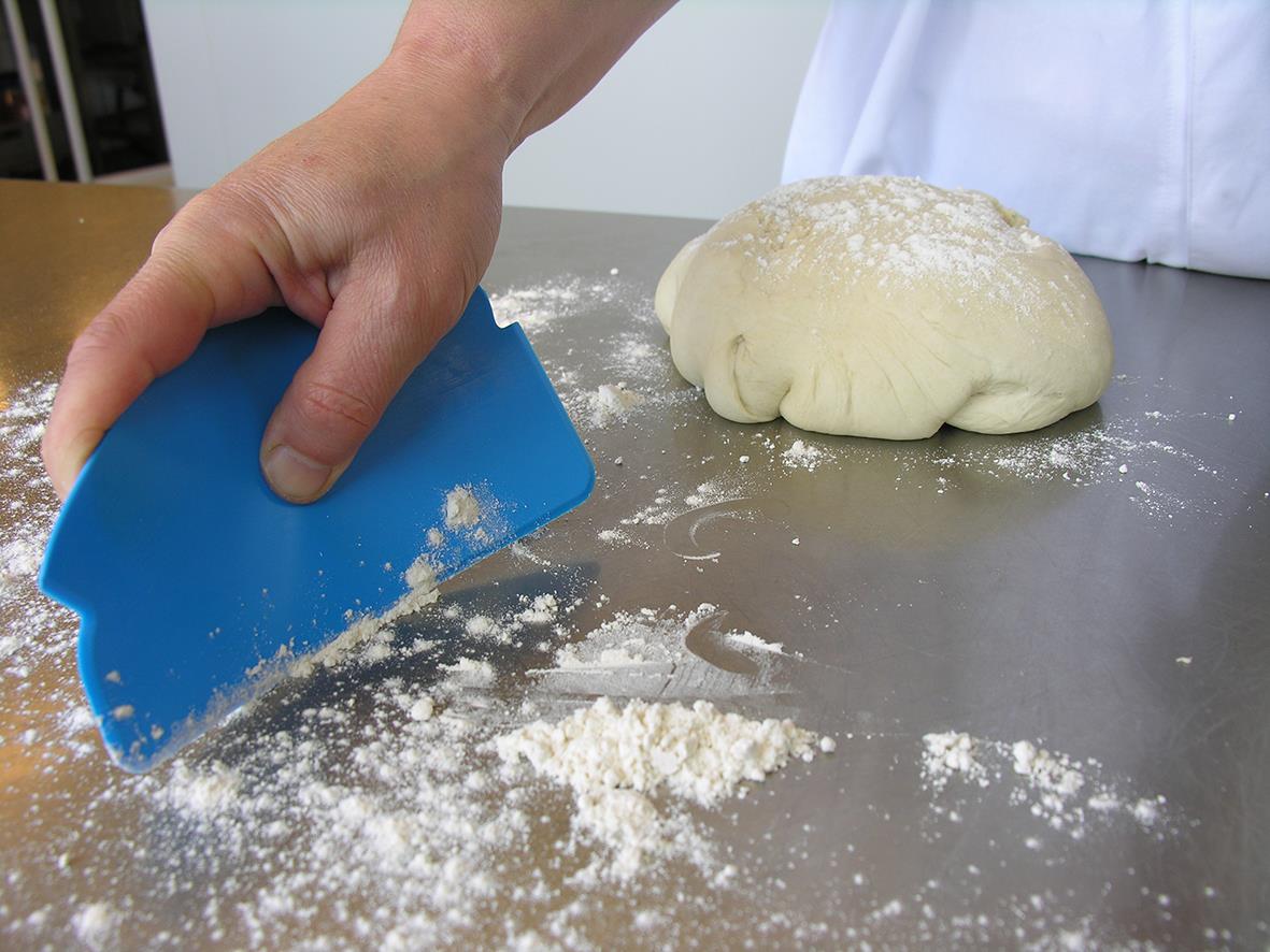 Person använder en blå handskrapa Vikan för att skrapa mjöl på ett bord