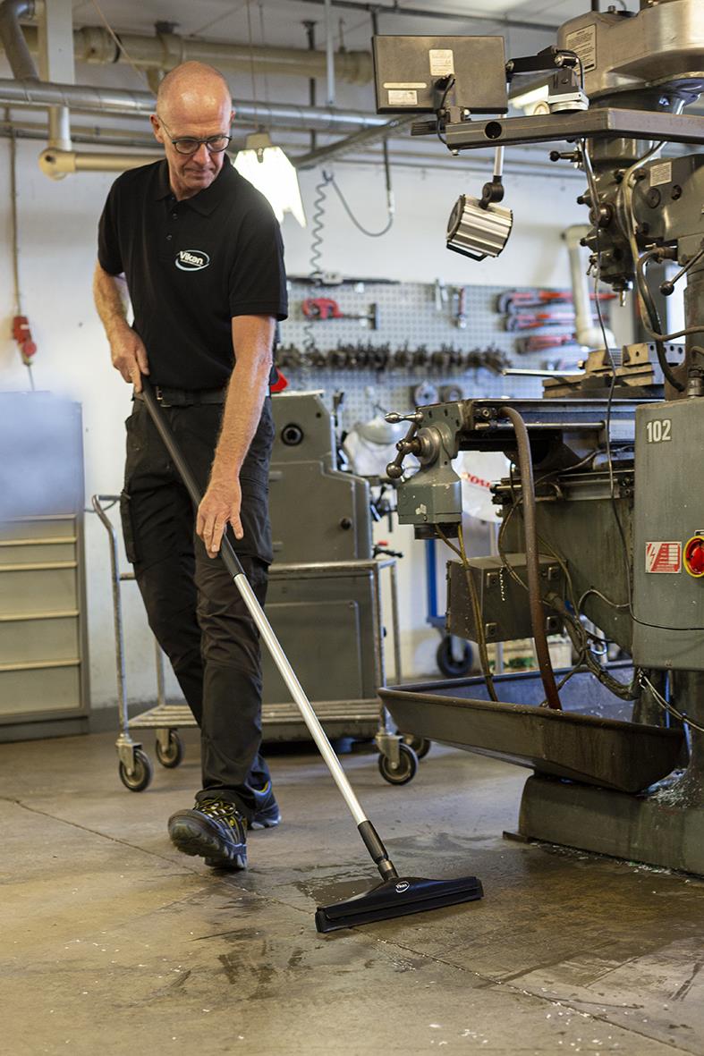 Man använder en golvskrapa för att rengöra golvet i en verkstad eller fabriksmiljö