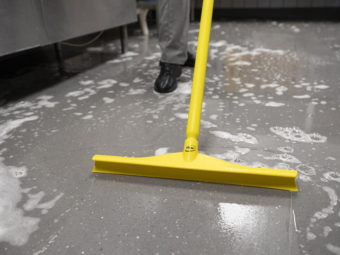 Golvskrapa Vikan Ultrahygienisk Gul 400mm används för att rengöra golv, med en person som sopar bort smuts och skum.