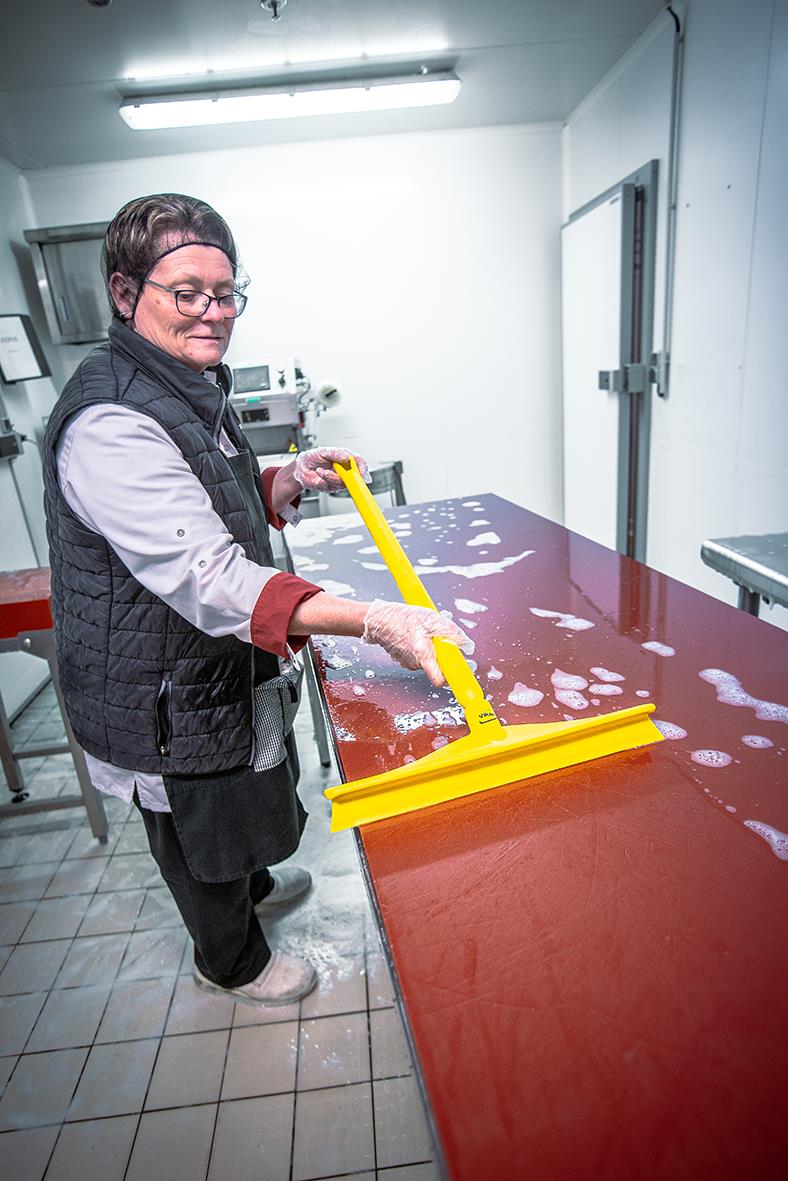 Person rengör ett bord med en gul golvskrapa Vikan Ultrahygienisk 400mm i ett kök eller rengöringsrum