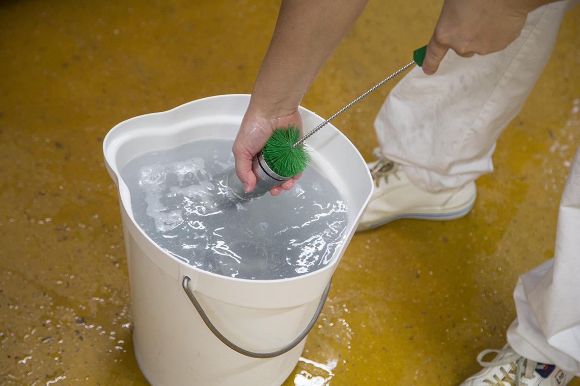 Person rengör en rörrensare Vikan Hård Vit 40x500mm i en hink med vatten