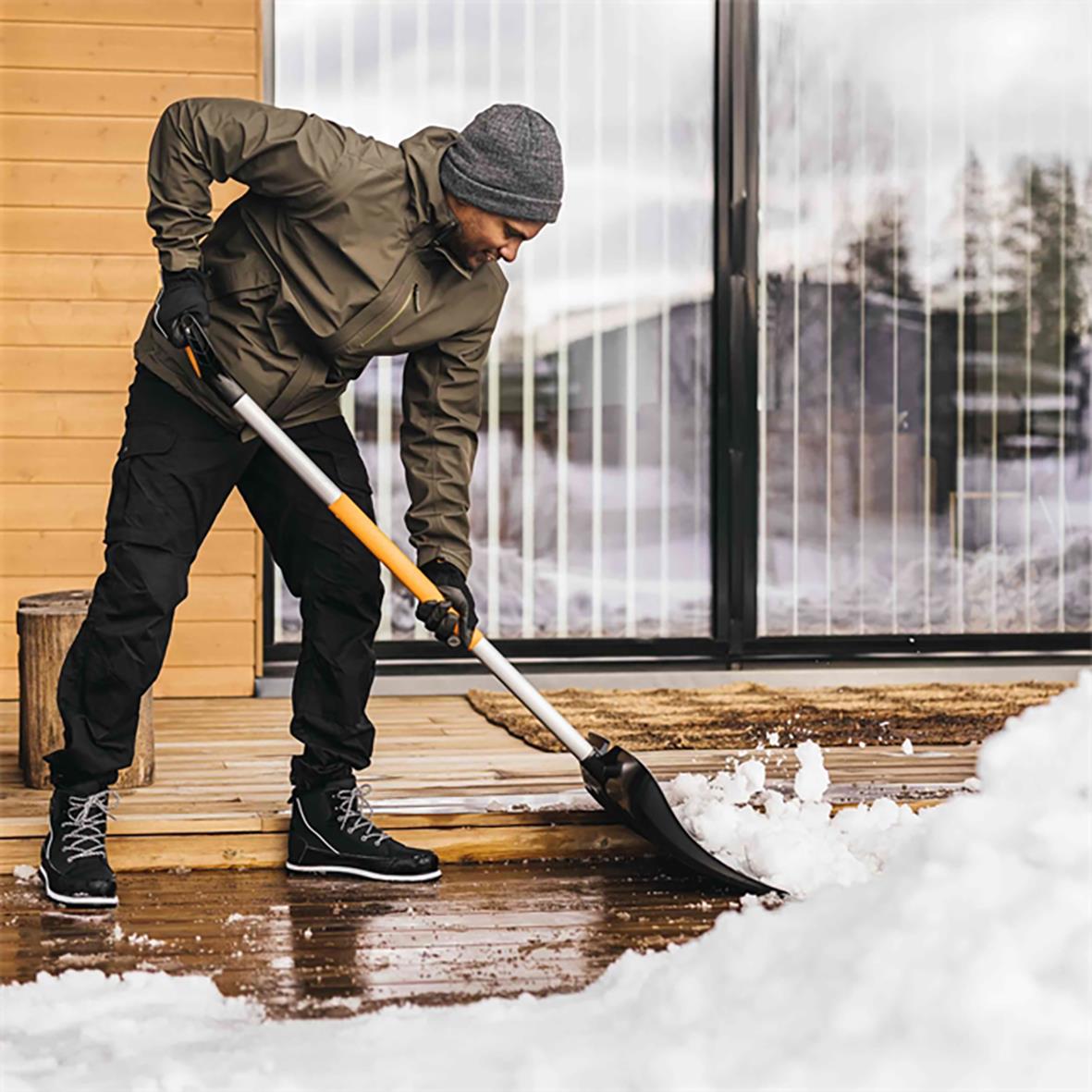 Man använder snöskyffel Fiskars X-Series för att skotta snö utomhus på en träterrass