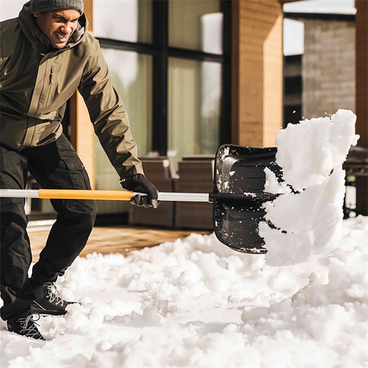 Person använder snöskyffel Fiskars X-Series Snöraka för att skotta snö utomhus