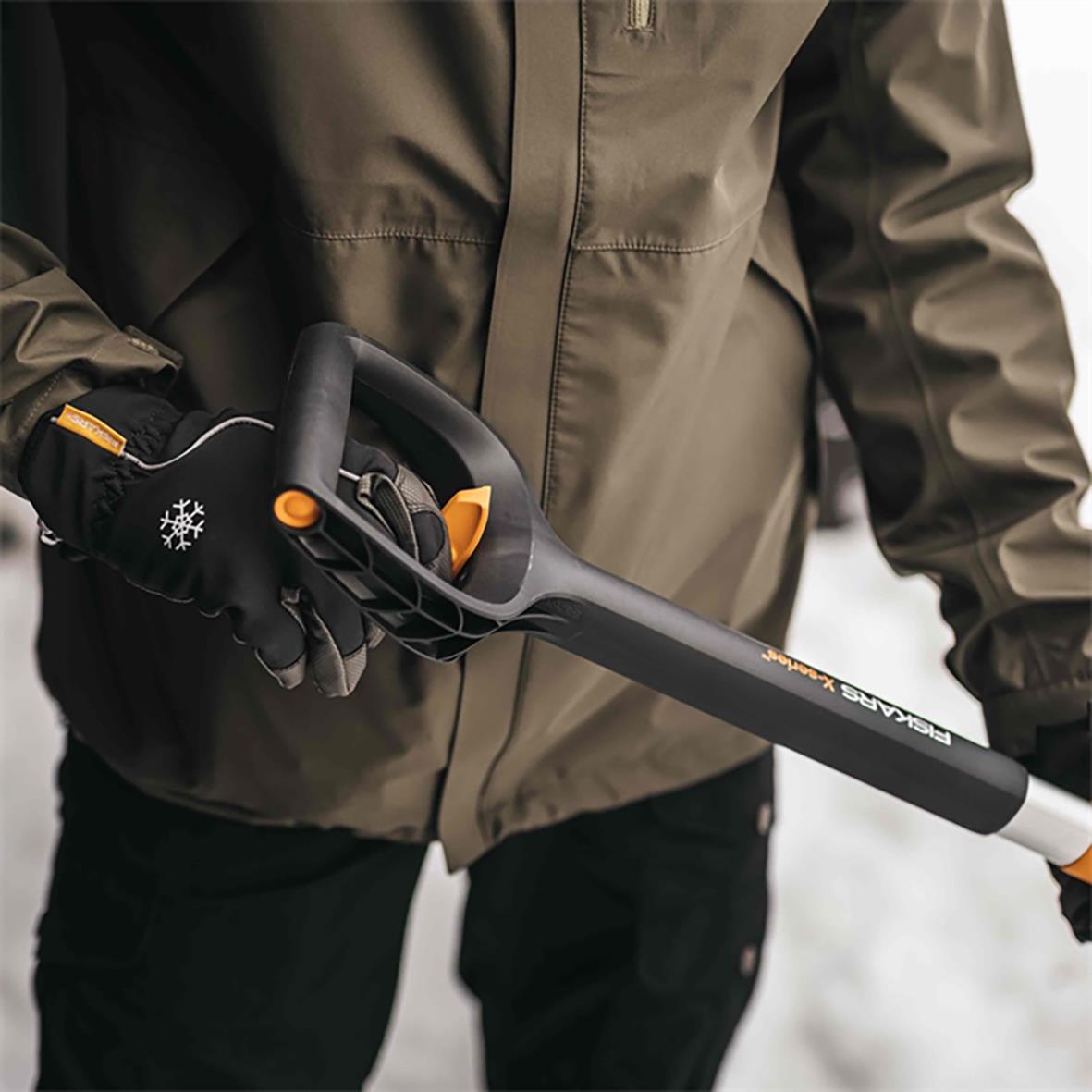Person håller en Fiskars X-Series teleskopisk snöskyffel med längd 79,5-98,7 cm, klädd i jacka och handskar