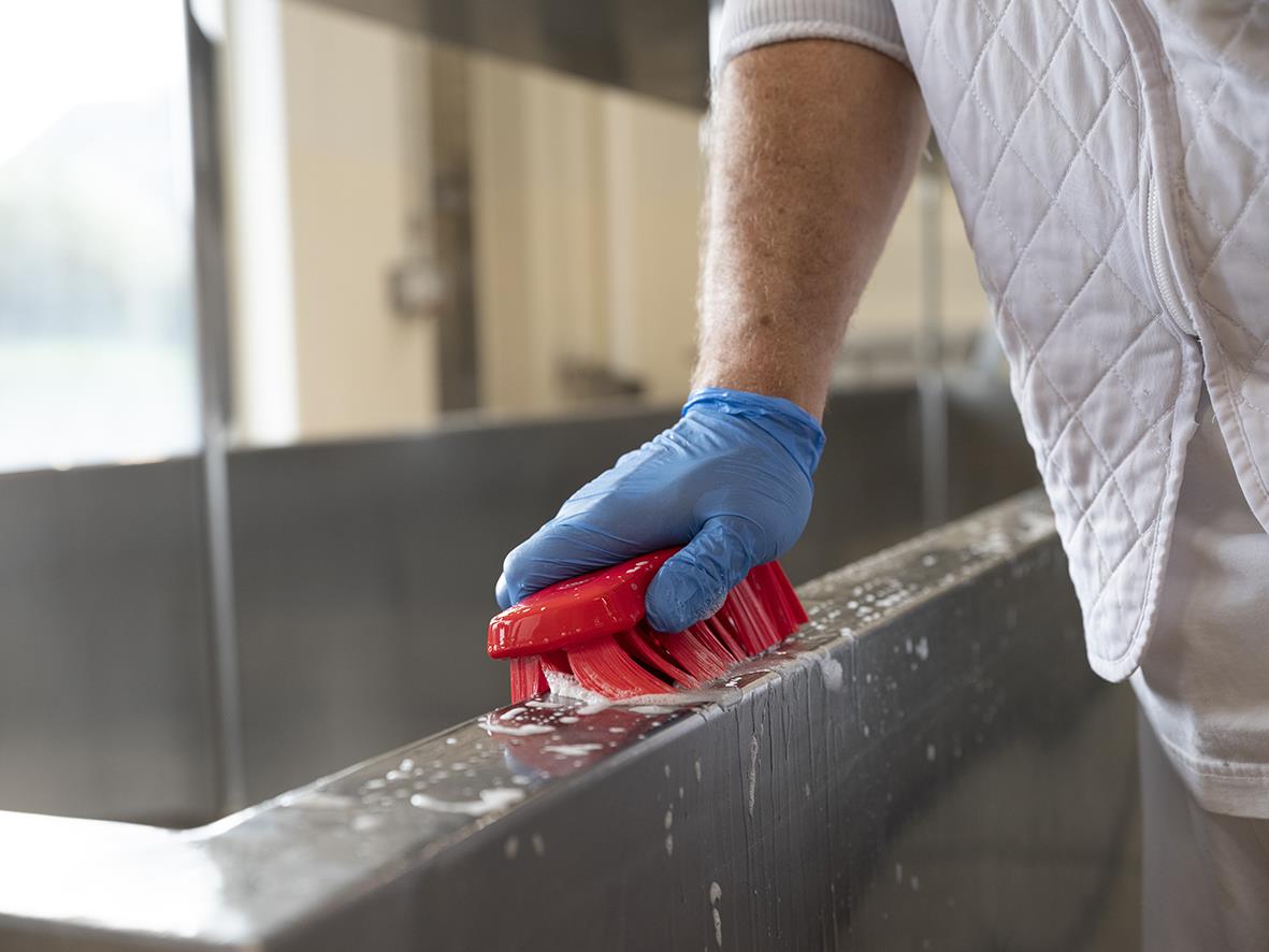 Person rengör en metallbänk med en röd handborste med blå handskar
