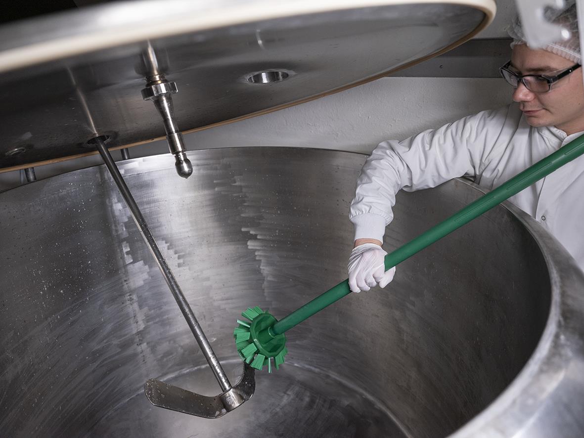 Person rengör stor tank med rosa hård tankborste i industriell miljö