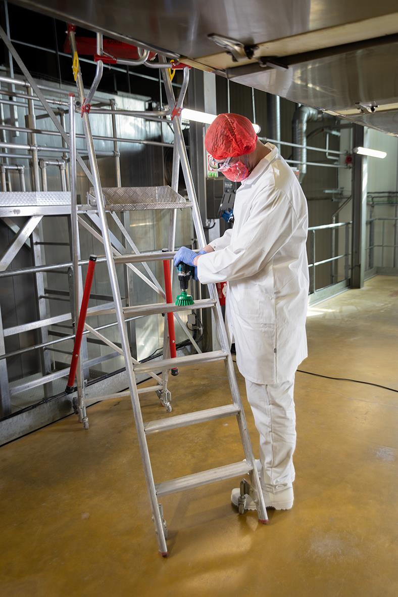 Person i skyddskläder och hårskydd rengör utrustning i industriell miljö