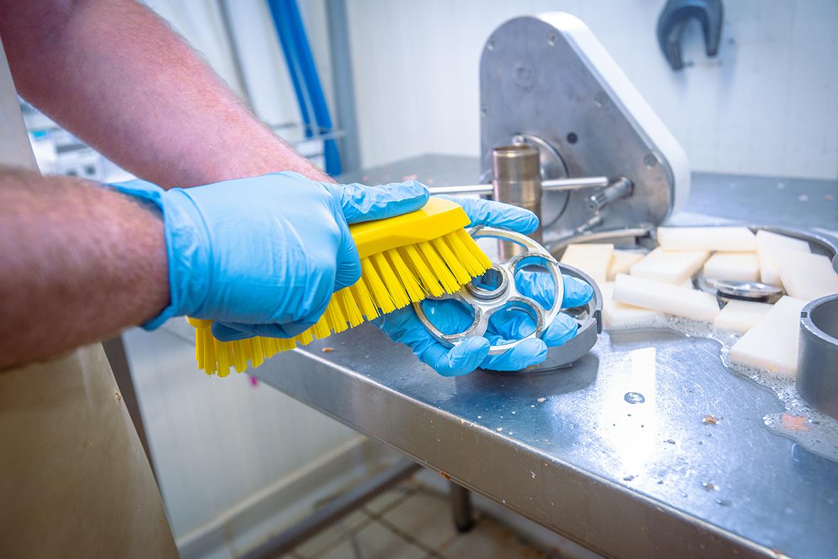 Person använder en stor gul hård handborste för rengöring i ett industriellt sammanhang