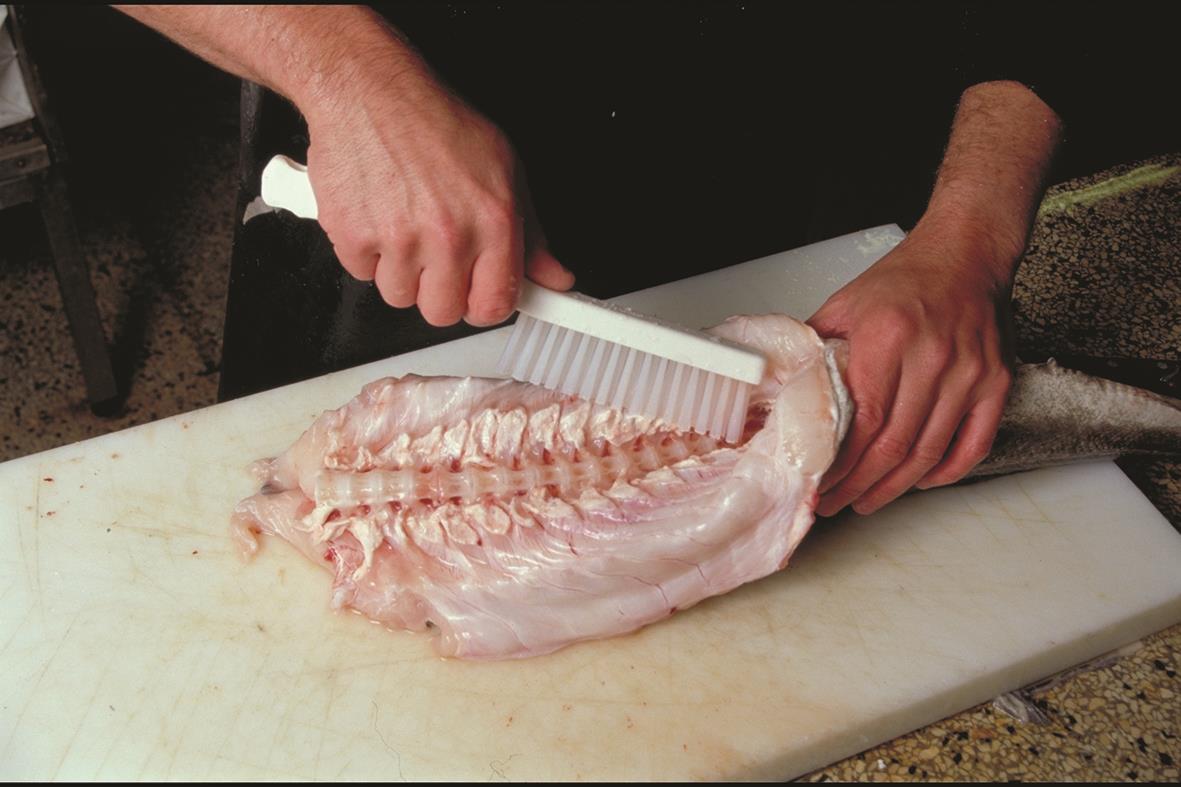 Person skär en fisk på en skärbräda med en tandad kniv, fokus på händer och fisk