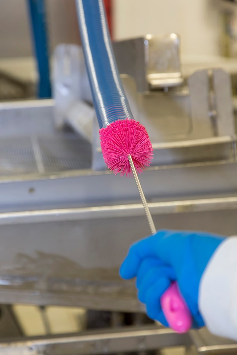 Rörrensare Vikan Medium Vit 60x510mm används för rengöring av rör, med rosa borst och blå handskar i ett industriellt kök eller laboratorium.