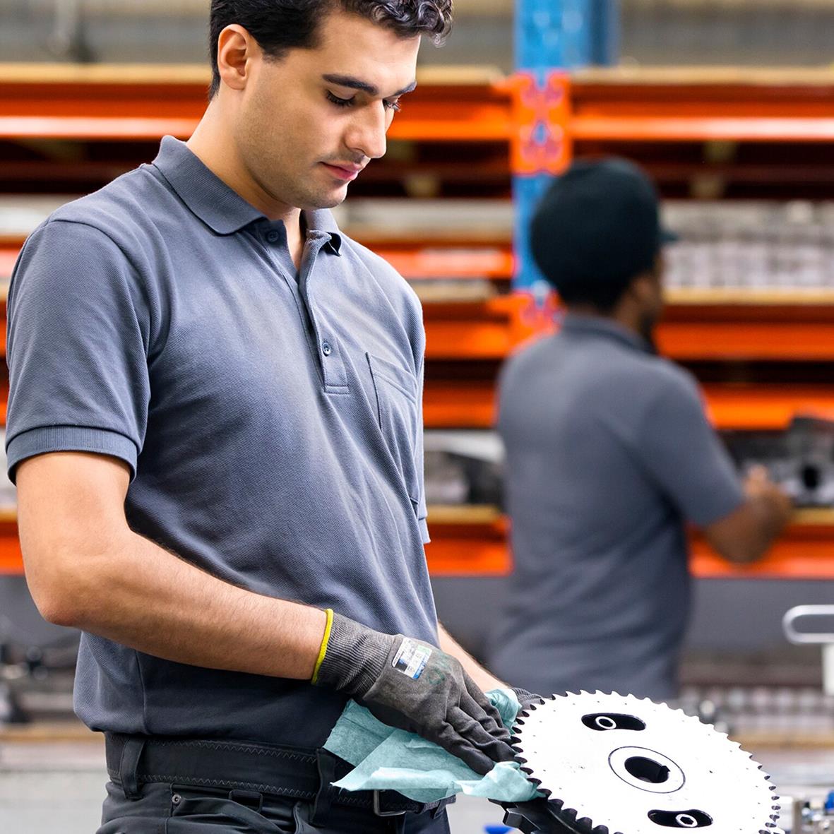 Man i fabriksmiljö använder rengöringsduk för att rengöra en metallskiva