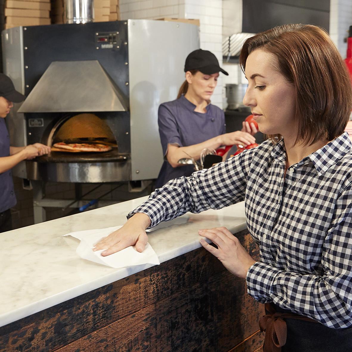 Kvinna torkar ett bord i ett kök med en rengöringsduk