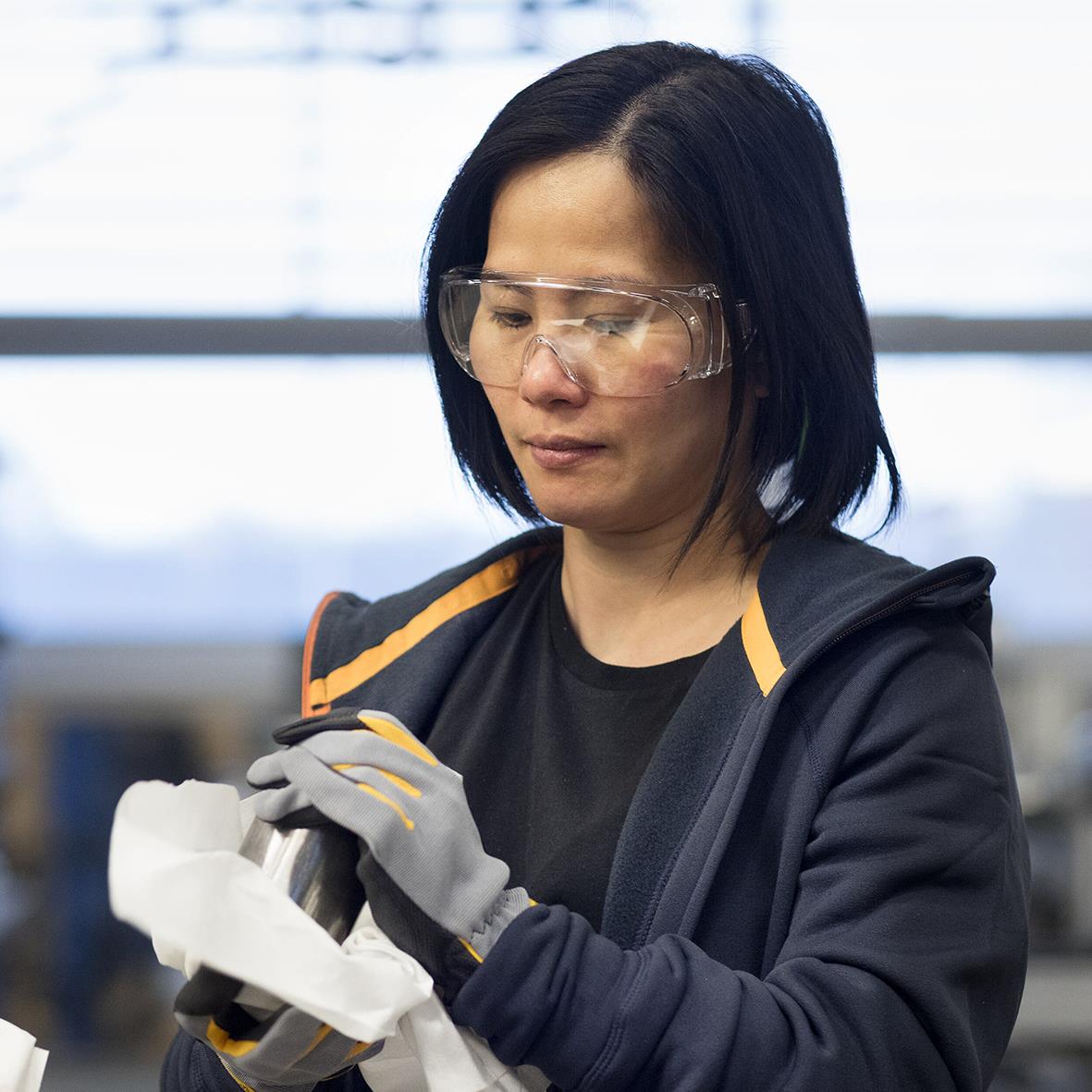 Kvinna i skyddsglasögon och handskar som använder rengöringsduk i industriell miljö